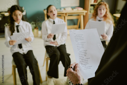 Εκτύπωση καμβά Children participating in choral practice by reading from sheets held by teacher