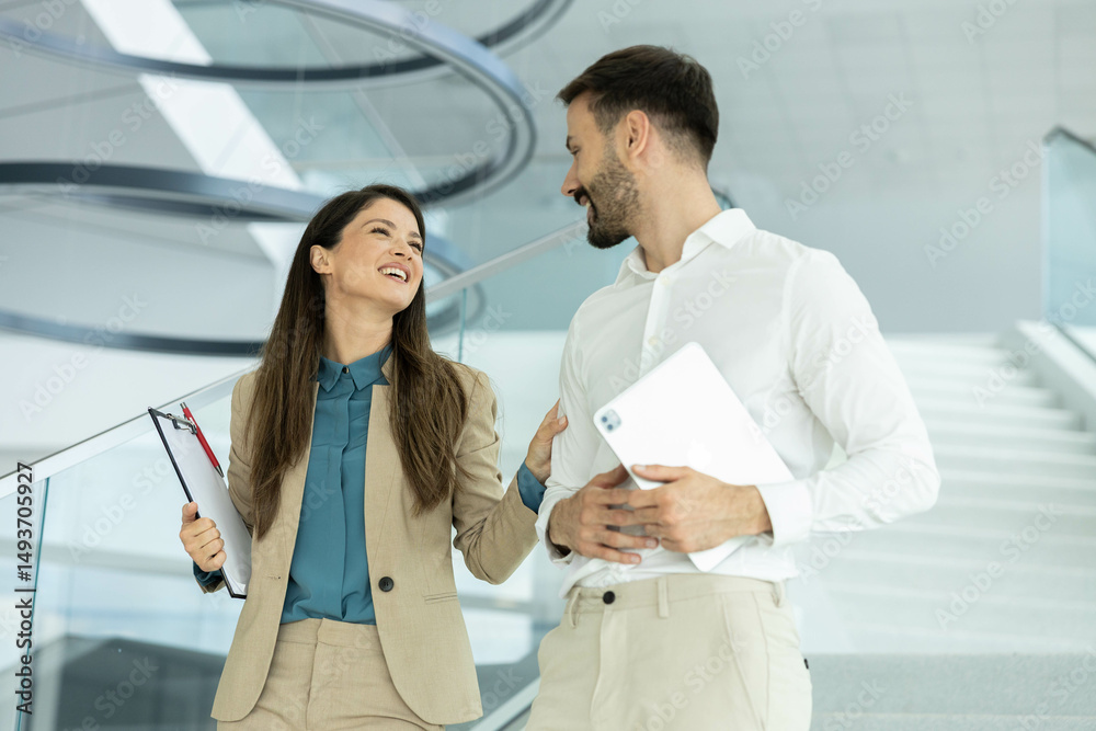 Fototapeta premium A woman and a man share a light-hearted conversation in a modern office, conveying warmth and professionalism.