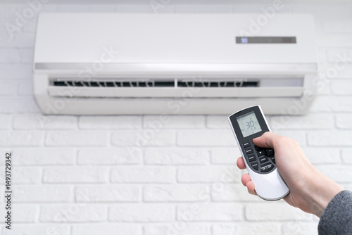 Air conditioner temperature adjustment with remote controller in room at home.