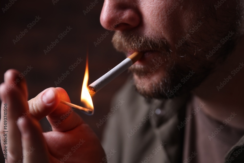 Fototapeta premium Man lighting cigarette with match on blurred background, closeup
