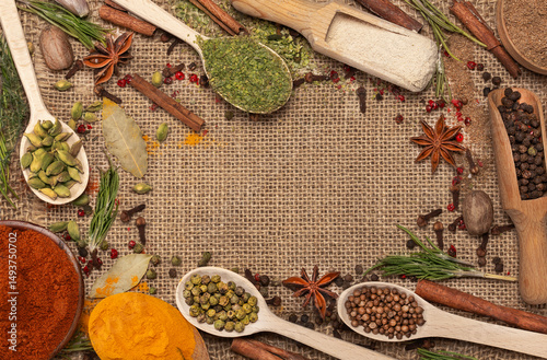 Background of multi-colored spices in spoons: turmeric, paprika, black and white pepper on rough burlap.