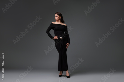 Young woman in stylish black dress on grey background
