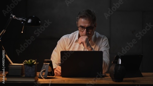 Businessman sitting at desk with laptop computer. Entrepreneur working late in office. Older, middle aged, mid adult, man in his 40s or 50s in business casual.