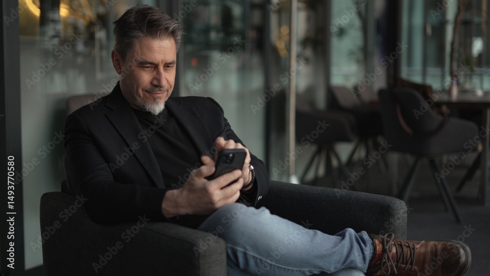© nyul - Businessman using phone in office. Middle aged man in business casual, Entrepreneur working online, reading finance report, thinking. .