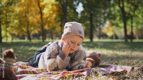A thoughtful and curious child is happily enjoying reading on a cozy blanket in a vibrant autumn park setting