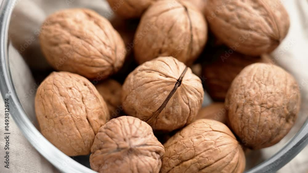 Full glass bowl with whole walnuts on fabric tablecloth. Close-up. Top view