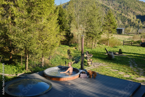 Young woman relaxing in a hot tub and looking at the beautiful mountain landscape. Thermal spa treatments in nature. Vacation outside the city