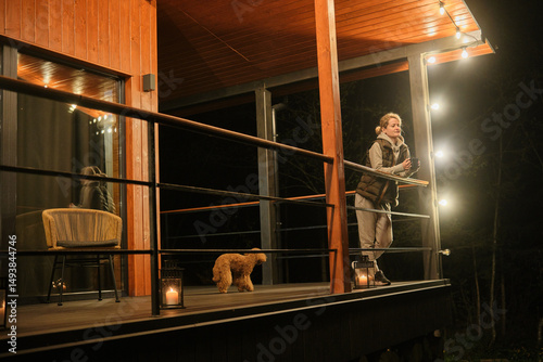 Young woman drinking tea on the veranda of a country house in the evening. Woman resting on the terrace of a house with a view of the forest. Vacation outside the city.