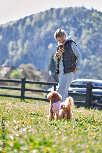 Young woman on a walk with a dog of the red-brown toy poodle breed. Walking with a pet.