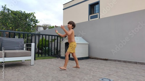 A boy in a yellow shirt is walking past a small white house