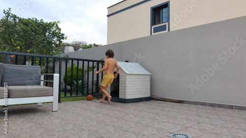 A boy in a yellow shirt and shorts is playing with a ball on a patio