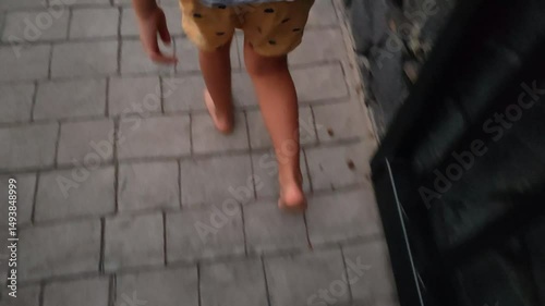 A person is walking barefoot on a brick sidewalk. The person is wearing yellow shorts. The image has a casual