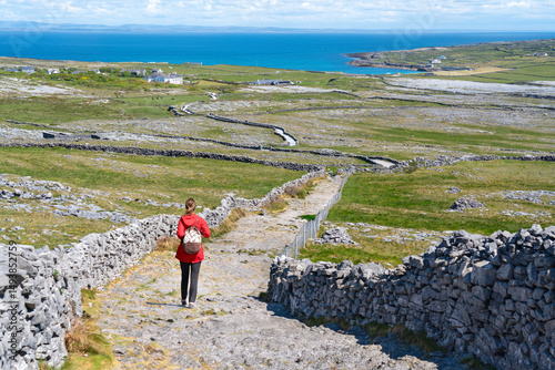 A tourist walking a trail on Inishmore with endless stone walls and the vast Atlantic stretching to the horizon.
