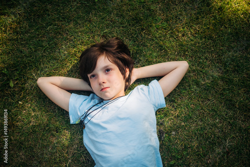 Smiling boy lying down with hands behind head on grass