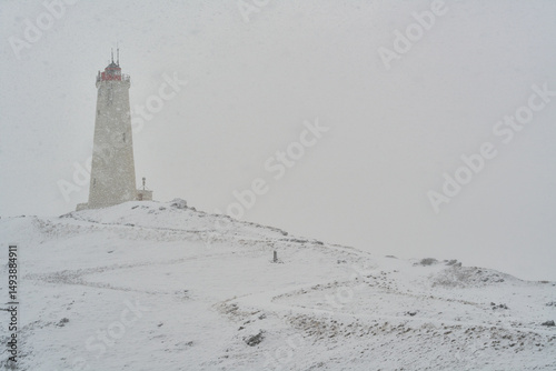 White lighthouse standing on snowy hill during snowfall