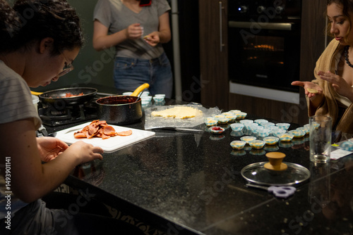 Three women collaborate in a kitchen, making food using dough and molds, capturing moments of teamwork and friendship. With copy space.