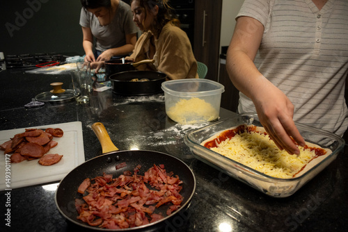 Three unrecognizable women collaborate in a kitchen, making pizza, food using dough and molds
