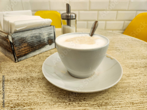 Cappuccino with a spoon in a white cup on a light table, Close up of cappuccino at cafe.
