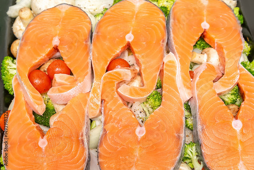 Raw fresh cut salmon fish steak slices on tomatoes,champignons mushrooms,broccoli vegetables, organic sea bass preparing for cooking,baking in stove.healthy diet food.