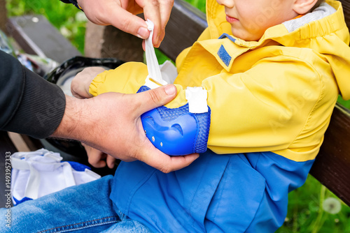 Dad puts fall protection on his son for roller skating,helping wears elbow pads.Sport,communication between parents and children,parenting,child care,family time together in city park