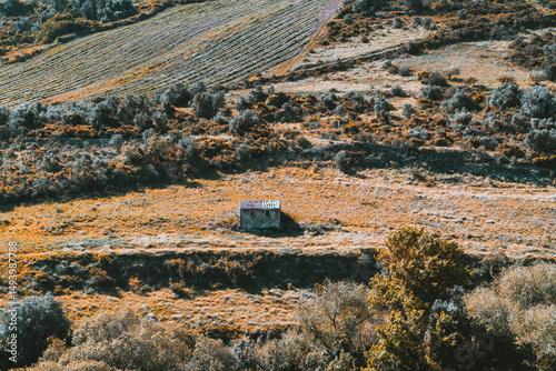 Wallpaper Mural Telephoto view of a solitary small abandoned stone hut with a rusty roof, surrounded by golden dry grass and rolling farmland fields, evoking isolation and rural tranquility Torontodigital.ca