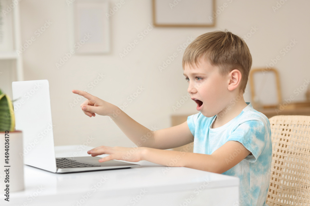 Surprised little boy pointing at modern laptop in living room Surprised little boy pointing at modern laptop in living room
