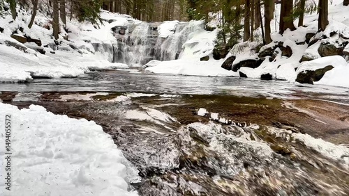 A stunning Winter Waterfall flows through a snowy forest, creating a breathtaking scene
