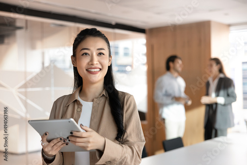 Asian businesswoman, marketing specialist, data analyst or female project manager holds tablet standing in modern corporate workspace. Business digital technology, innovations, and professional growth