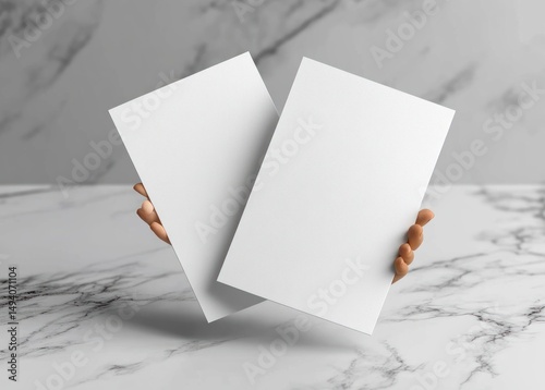 Two hands holding two blank white rectangular papers against a blurred marble background showing clean sheets ready for text or design