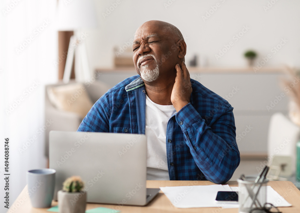 Naklejka premium Neckache. Senior African American Man Touching Aching Neck Suffering From Pain Sitting Working On Laptop In Modern Office. Healthcare, Health Problems In Older Age Concept