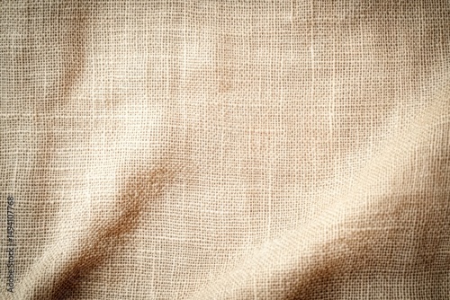 Close-up texture of beige woven fabric with visible fibers and natural light creating soft shadows and folds