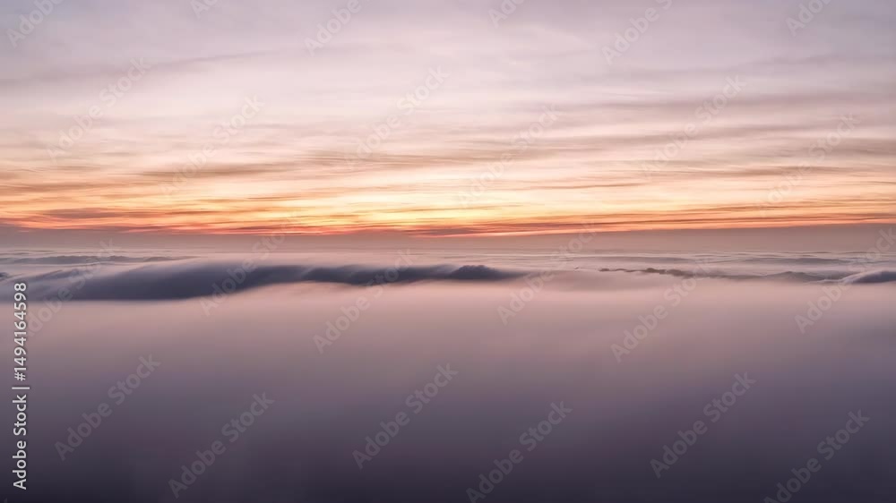 Dramatic scenery of dark rippled water meeting thick fog bank under pastel gradient sunrise sky, displaying atmospheric perspective and ethereal mood