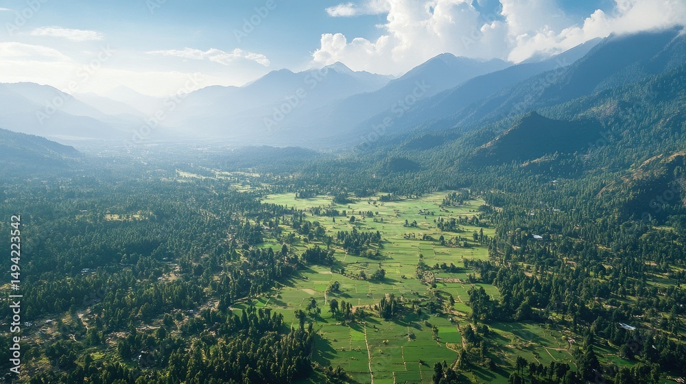 Fototapeta premium Aerial View of Lush Green Valley Surrounded by Majestic Mountains Under Bright Blue Sky and Soft White Clouds in Scenic Landscape
