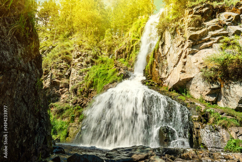 View of the seething stream of falling water of the Kamyshlinsky waterfall on a sunny summer day in the Altai Republic, Russia