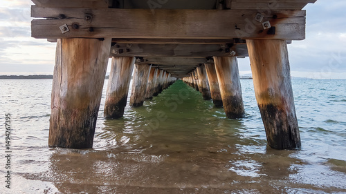 Diminishing perspective of water and wooden pylons underneath a jetty