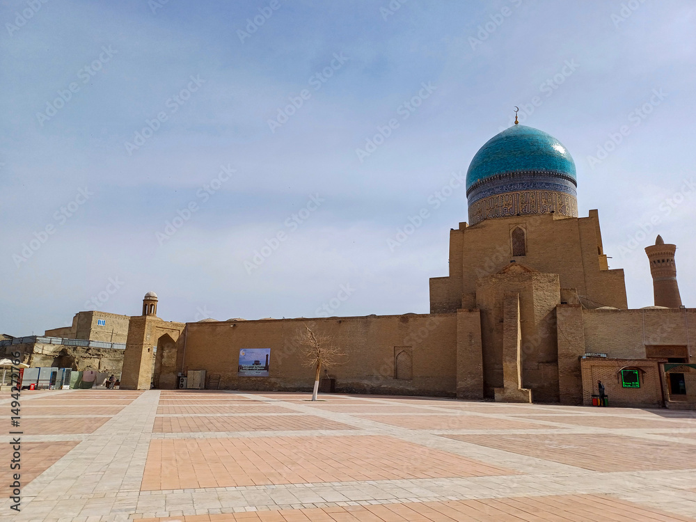 Fototapeta premium Kalon Mosque and the towering Kalyan Minaret in Bukhara, Uzbekistan. The mosque, with its large blue dome, stands adjacent to the minaret, a slender brick tower that dominates the blue skyline