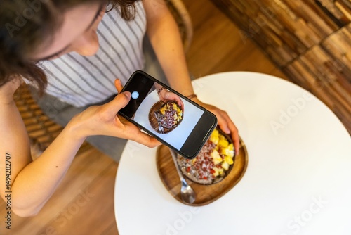 Woman taking photo of acai bowl with smartphone in cafe.