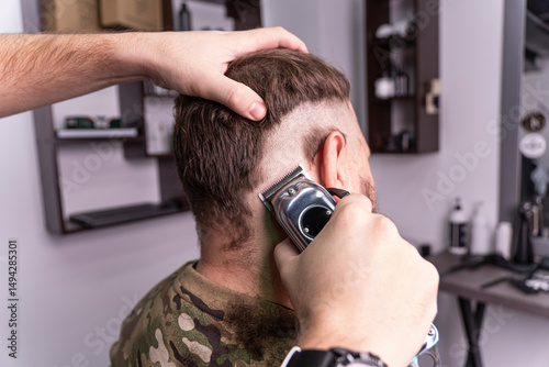 фотографія young man in a military uniform shaves his head bald for military service