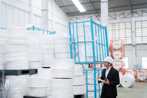 During a routine audit, the European male engineer reviews plastic output data from the industrial plant, identifying areas where the business can cut unnecessary costs.