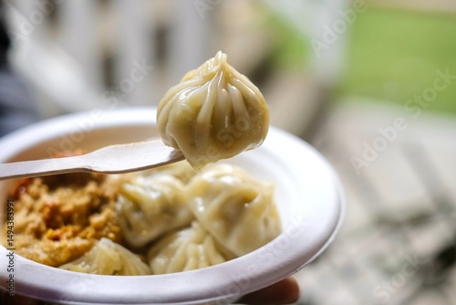 Close-up of a chicken momo on a fork with a plate of assorted momos served with spicy chutney at a Nepalese street food stall in Little India - Harris Park, Sydney, New South Wales, Australia 