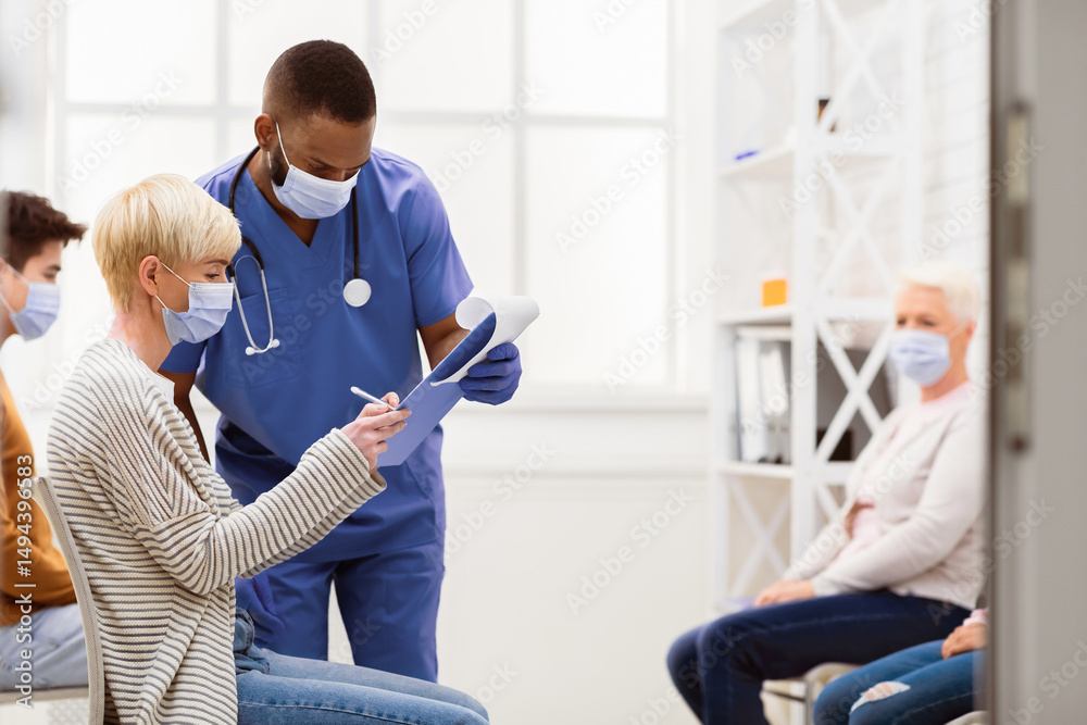 Obraz premium Patient Woman Signing Papers With Doctor Before Coronavirus Vaccination Sitting In Hospital Waiting-Room. Covid-19 Pandemic Medical Treatment Concept. Empty Space For Text