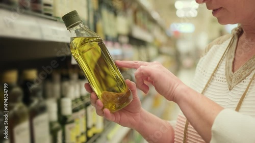 Woman reading label on bottle of olive oil in supermarket before buying.
