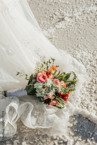 Bridal Bouquet on lace dress spread over white sandy ground.