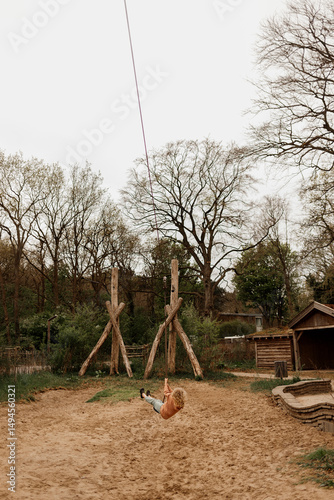 Child swinging on a long zip line in a rustic outdoor playground