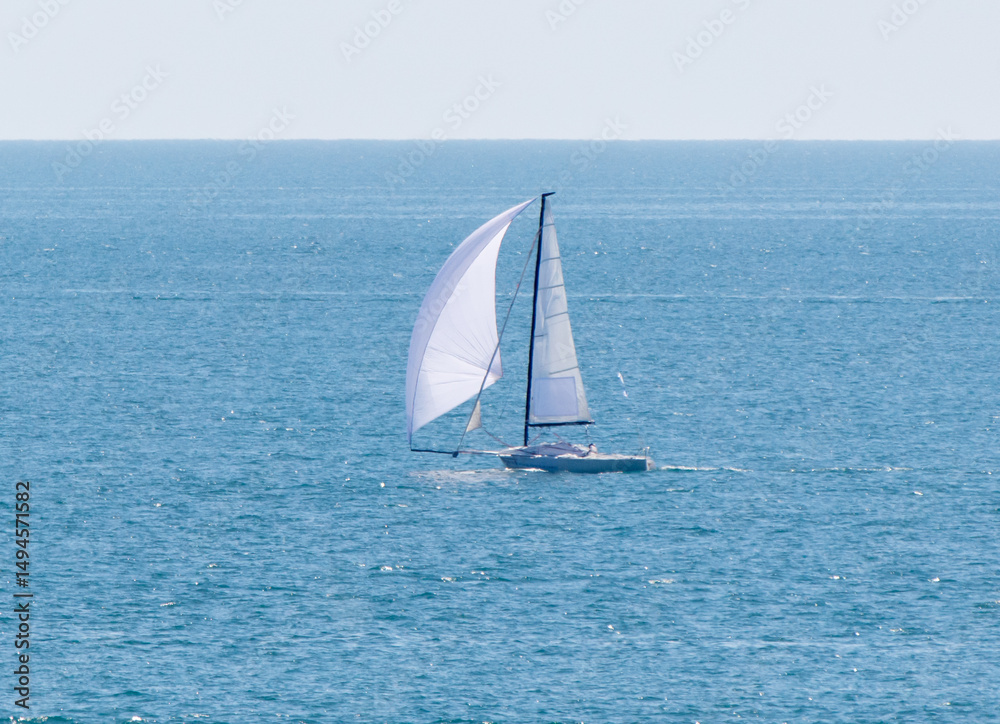 Fototapeta premium A sailboat is sailing in the ocean with a white sail