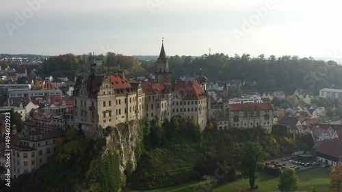 Wallpaper Mural Aerial drone footage revealing the majestic Hohenzollern Castle in Sigmaringen, Germany. The historic structure rises above the town and the Danube River, surrounded by lush greenery and classic Europ Torontodigital.ca