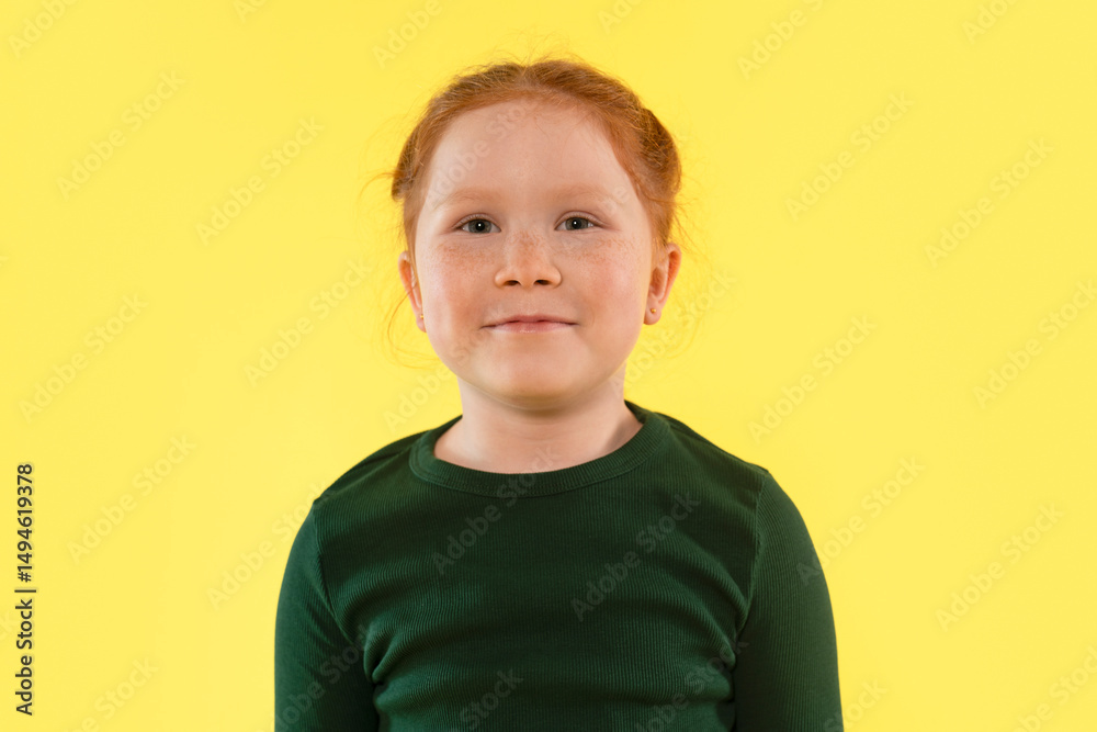 Young girl with red hair smiles against a bright yellow background showcasing her joyful personality and lively spirit during a portrait session Young girl with red hair smiles against a bright yellow background showcasing her joyful personality and lively spirit during a portrait session