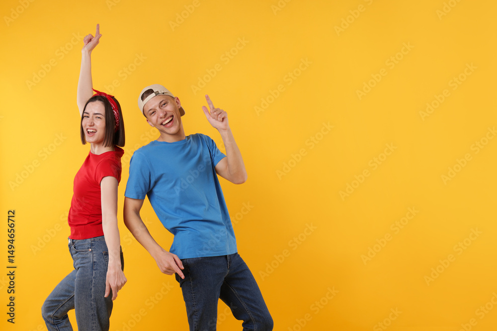 Obraz premium Happy couple in stylish clothes dancing on yellow background. Space for text