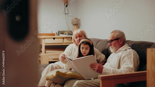 Granddaughter laughing while looking at photo album with grandparents, they are sitting on sofa