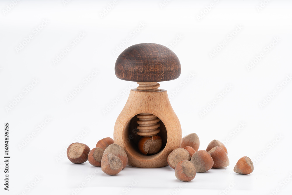 Wooden mushroom-shaped nutcracker surrounded by hazelnuts, with one nut placed inside for cracking. Isolated on white background.. Wooden mushroom-shaped nutcracker surrounded by hazelnuts, with one nut placed inside for cracking. Isolated on white background..